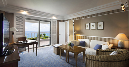 Image of a Premier Suite with beige-toned interiors, a sofa, a table, and a balcony.